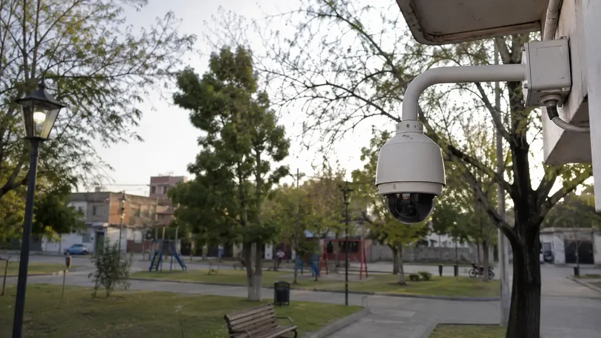 Una cámara de vigilancia genérica en una esquina en una plaza de barrio con mobiliario urbano, plano medio documental